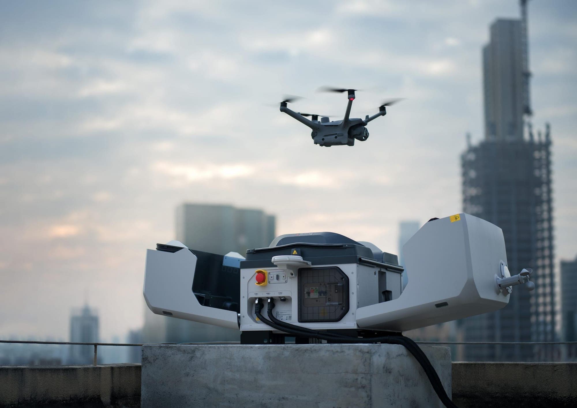 La station du drone ouverte sur un toit, au crépuscule, et le drone qui vient d'en décoller.